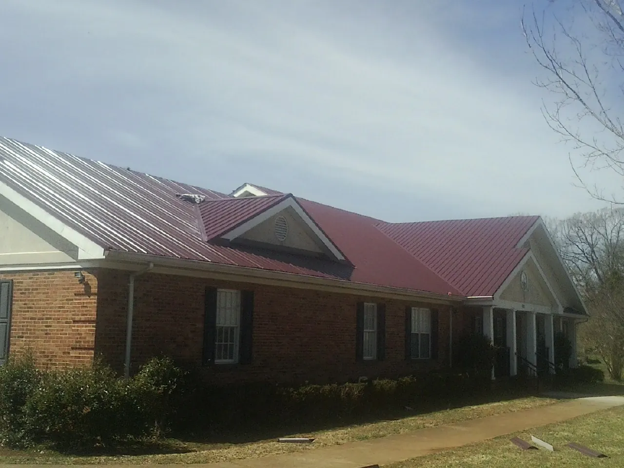 Red metal roof with gabled entries on a long brick building, from a Hail Damage Roof Repair job in Woodlake