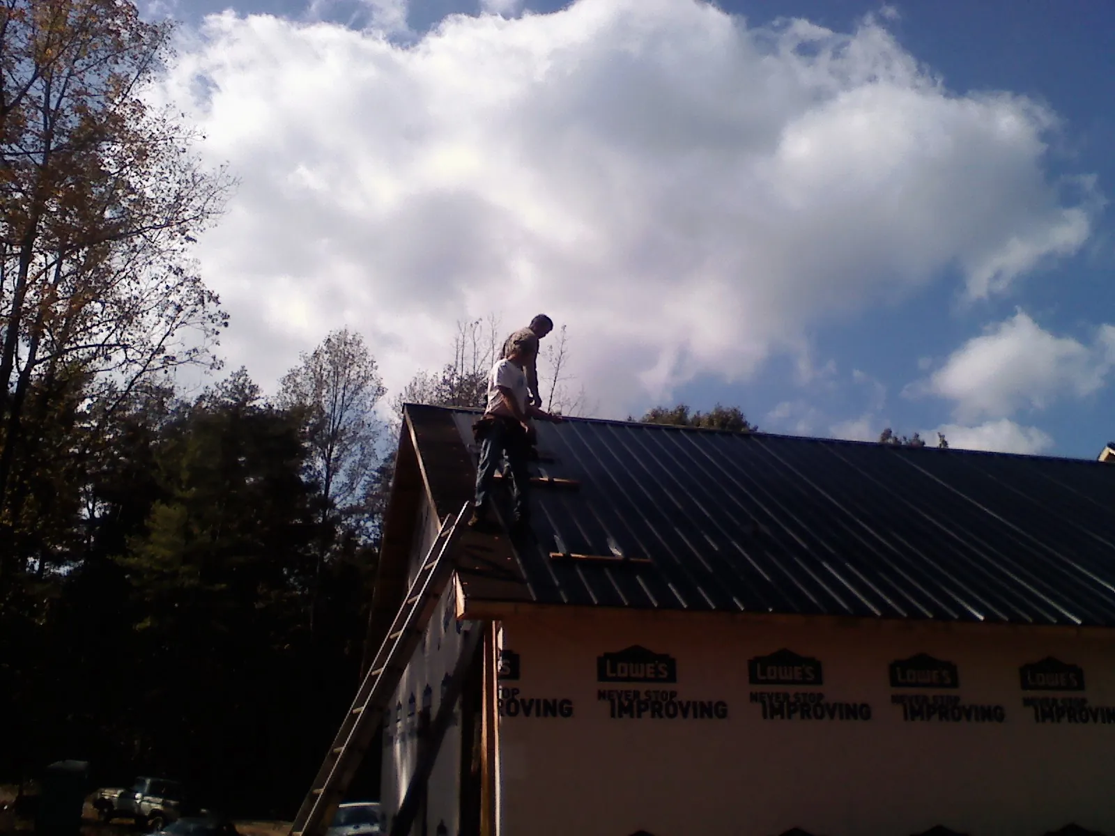 Roofer fastening dark metal panels high against a cloudy sky, from a Roof Inspection job in Woodlake