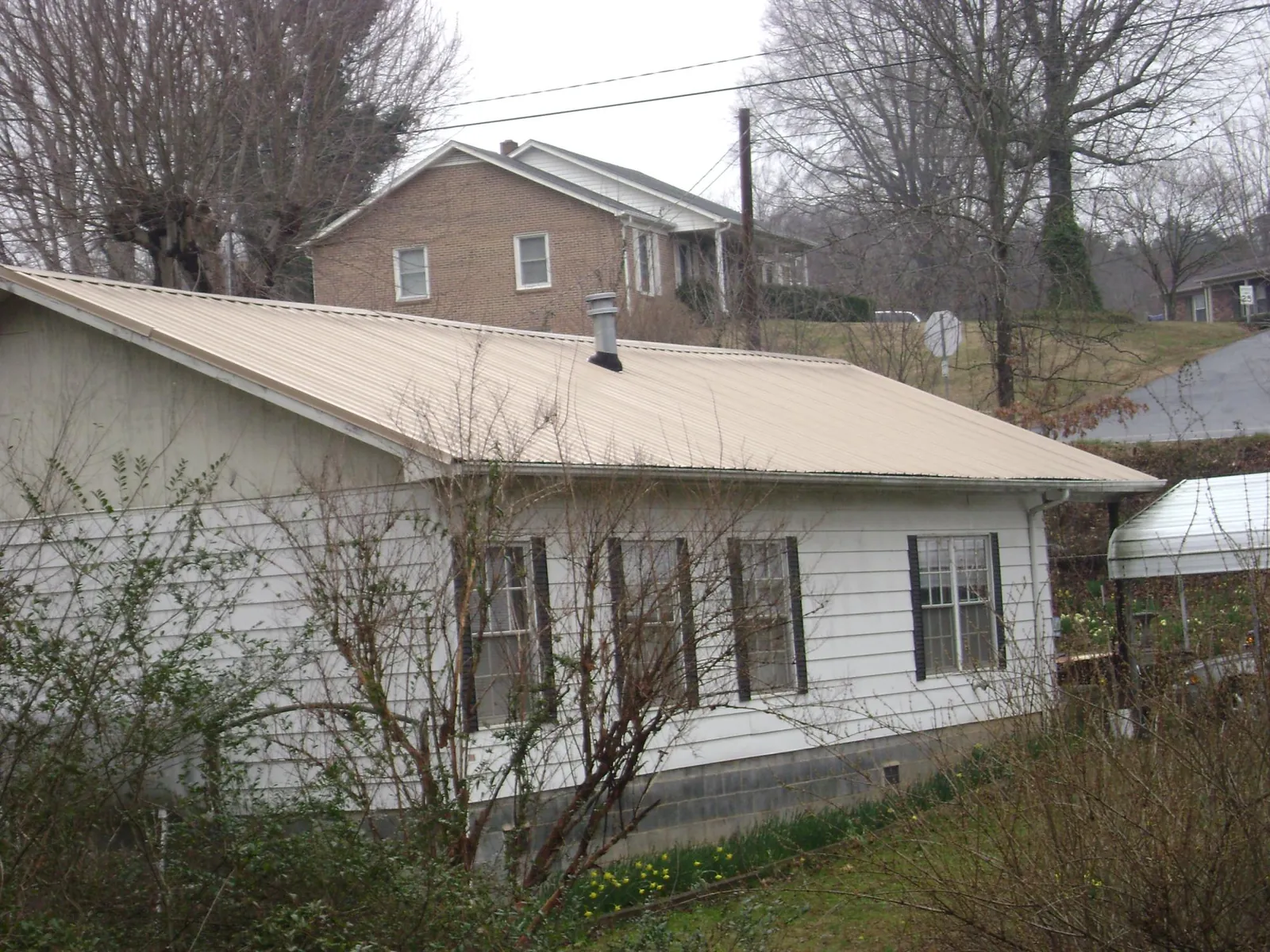 Tan metal roof on a white sided house set into a hillside — Commercial Roofing by Roofing Brothers in Woodlake
